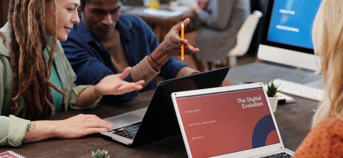 Diverse team collaborating with laptops in a modern office setting, discussing digital evolution.